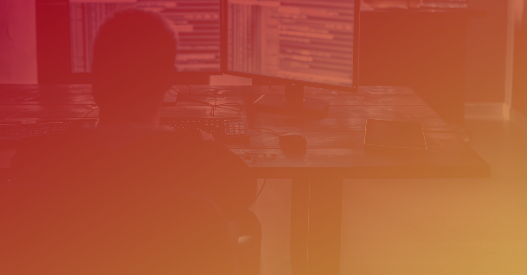 Silhouette of a person at a computer desk, dual monitors displaying code or data