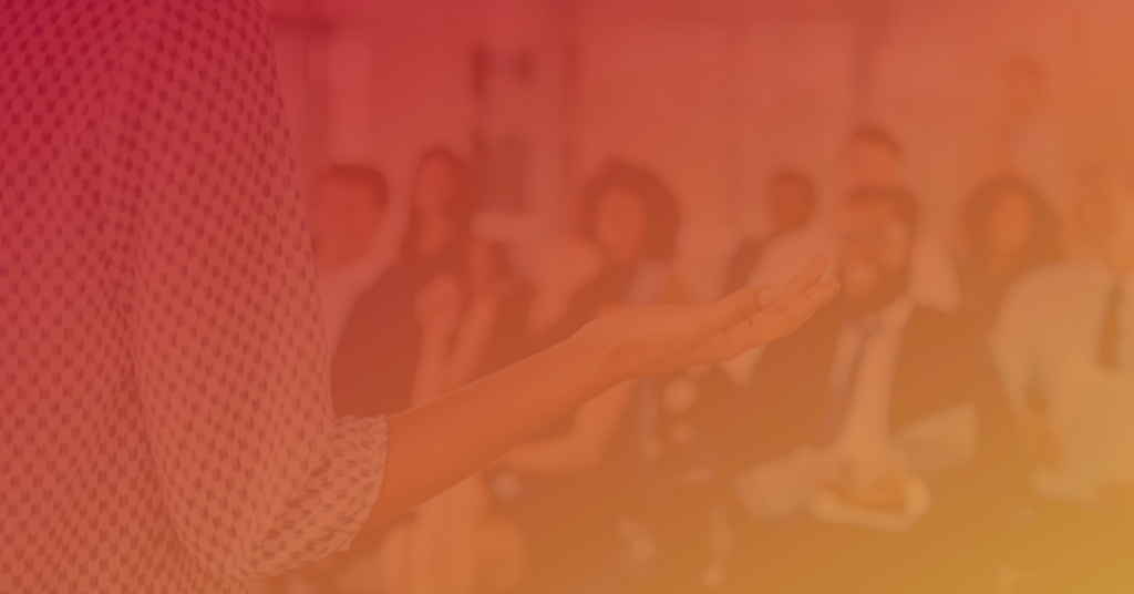 Person gesturing while speaking to a blurred audience, warm filter applied