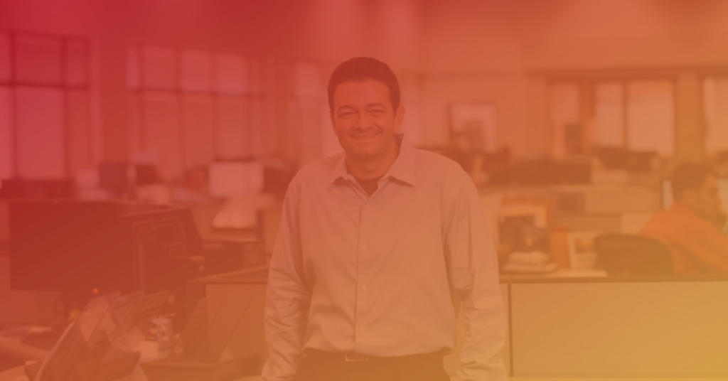 Rick-Trujillo is smiling, standing in a modern office with a warm orange-red overlay